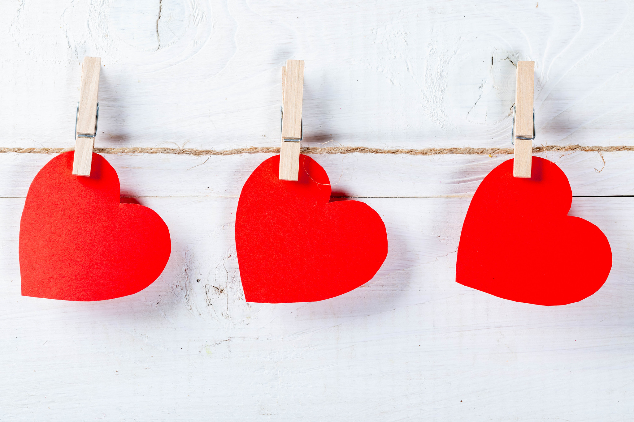 three red paper hearts pegged to string against white wooden background